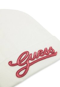 Berretto lavorato a maglia bianco con un prominente logo "Guess" ricamato in rosa. Texture morbida e vestibilità aderente. Design pulito e minimale.