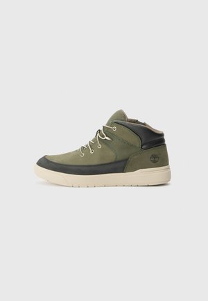 Baskets montantes vertes et noires en matériaux suédine et synthétiques, à bout rond, avec des accents texturés et une semelle en caoutchouc. Logo Timberland au niveau du talon.
