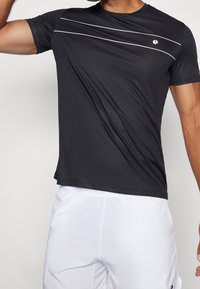 Camiseta atlética negra de mangas cortas, con rayas horizontales blancas en el pecho y una tela texturizada.