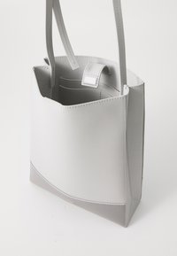 Grå skinn totebag med en jevn finish, rektangulær form, doble hanke og en subtil logo aksent nederst. Innvendig inkluderer lommer.