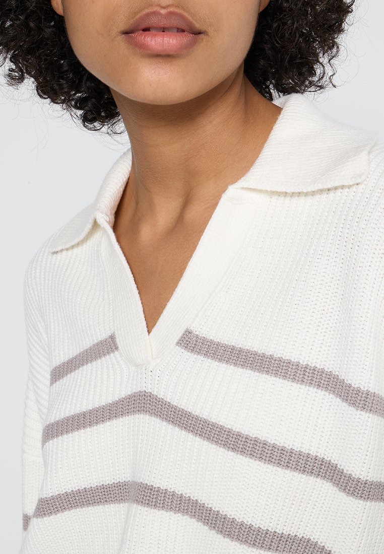 Białe sweter z dzianiny z dekoltem w kształcie litery V, z poziomymi jasnoszarymi paskami. Materiał ma teksturowane wykończenie i luźny kołnierz.