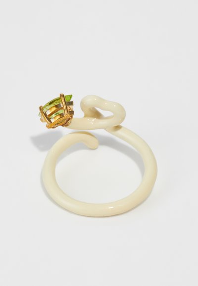 Inel din ceramică de culoare crem, cu un design răsucit, prezentând o gemă verde fixată în accente de metal aurii. Textură netedă pe întreaga suprafață.