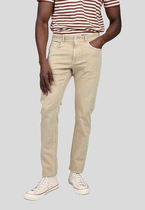 Pantalons en coton beige avec une coupe slim, présentant un design classique à cinq poches. Associés à des baskets blanches et un t-shirt rayé.