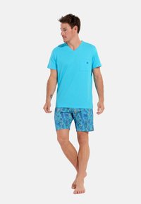 T-shirt en coton bleu clair à col en V avec une poche sur la poitrine, associé à un short de bain bleu à motifs avec des feuilles tropicales en vert et jaune.