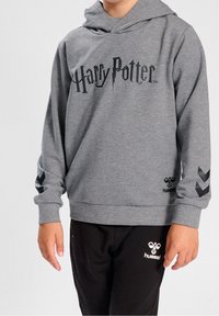 Felpa grigia con logo "Harry Potter" in nero, caratterizzata da maniche lunghe e polsini a costine. Pantaloni tuta neri con logo bianco sull'anca.