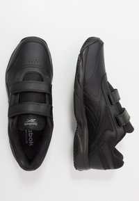 Zapatillas deportivas negras con dos correas de velcro, parte superior de material sintético suave, laterales texturizados y suelas de goma diseñadas para la comodidad y la tracción.