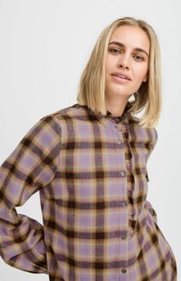 Chemise à manches longues à carreaux dans les tons violet, marron et beige. Présente un un bouton à l'avant, un léger volant au col et une coupe décontractée. Texture douce.