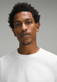 Vit sweatshirt med rund halsringning och mjuk textur, med ribbat halsband och något figurnära design. Svart lockigt hår och naturlig hudton.