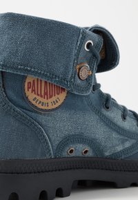 Botte Palladium en toile bleue avec col rabattable, œillets métalliques, coutures visibles et semelle en caoutchouc à crampons en gros plan.