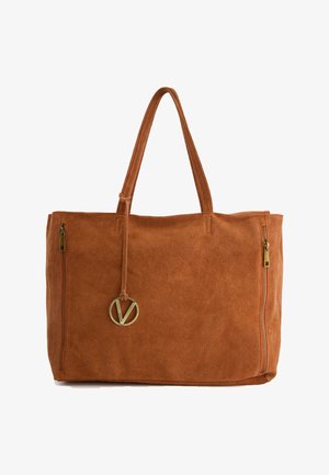 Brown suede tote bag with two zippered pockets, long handles, and a gold circular logo accent attached by a leather strap.
