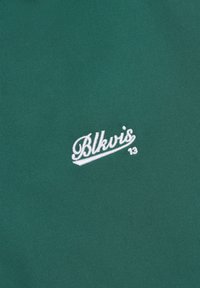 Tissu vert avec texte brodé en blanc "Blkvis 13" en écriture cursive centré sur la surface.