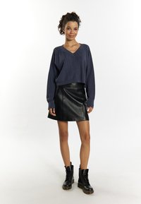 Maglione di lana blu navy con scollo a V, caratterizzato da un motivo a diamante testurizzato; abbinato a una mini gonna di pelle nera e stivali neri con lacci.