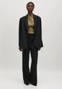 Schwarzer maßgeschneiderter Blazer über einem beigen enganliegenden Top, kombiniert mit schwarzen weit geschnittenen Hosen und spitzen schwarzen Absatzschuhen; glattes Material und strukturierte Silhouette.