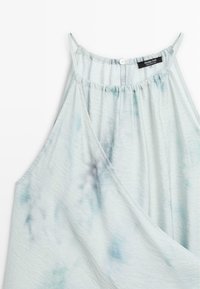 Blouse sans manches tie-dye bleu clair avec fines bretelles, encolure froncée et petit bouton blanc au dos du col.