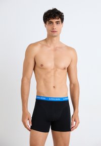 Schwarze Boxer Shorts mit einem blauen Bund, der das "BJÖRN BORG"-Logo trägt. Glattes Material, eng anliegendes Design und Oberschenkellänge.