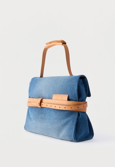 Τσάντα ώμου από μπλε τζιν ύφασμα με λουρί και διακοσμητική ζώνη από ανοιχτό καφέ δέρμα, όρθια σε απλό λευκό φόντο.