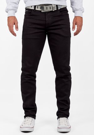 Jean en denim noir à coupe ajustée, doté d'une ceinture grise et associé à des baskets blanches à lacets bas. Texture lisse, design classique à 5 poches.