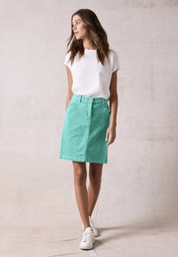 Una gonna in corduroy verde menta con taglio dritto, due tasche frontali e chiusura con bottone. Abbinata a una maglietta bianca a maniche corte e sneakers bianche.