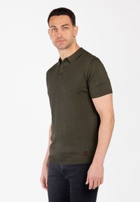 Olivgrünes Polo-Shirt mit kurzen Ärmeln, einem gerippten Kragen und Bündchen, einer Knopfleiste mit drei Knöpfen und einem kleinen Logo-Patch am Saum.