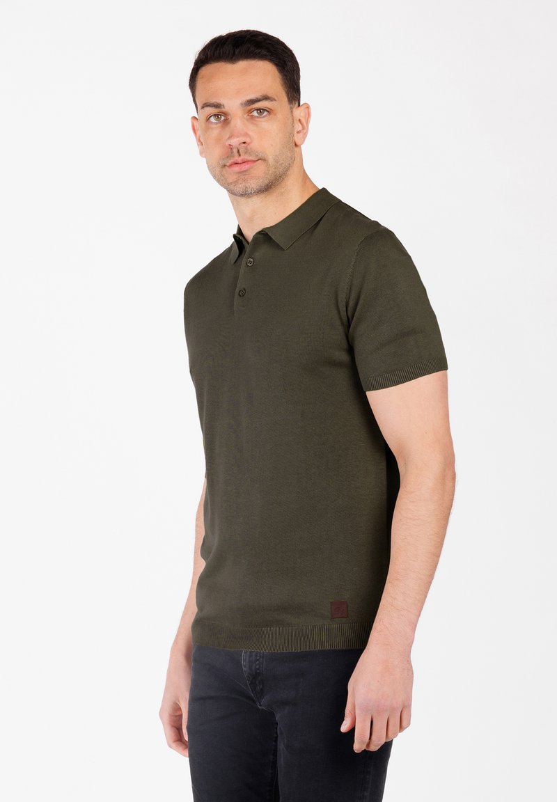 Olivgrünes Polo-Shirt mit kurzen Ärmeln, einem gerippten Kragen und Bündchen, einer Knopfleiste mit drei Knöpfen und einem kleinen Logo-Patch am Saum.