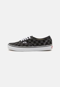 Baskets Vans noires avec lacets blancs, semelle blanche et motif à damier avec le texte "VANS" imprimé sur tout le tissu.