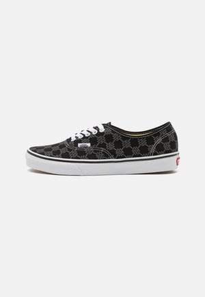 Baskets Vans noires avec lacets blancs, semelle blanche et motif à damier avec le texte "VANS" imprimé sur tout le tissu.
