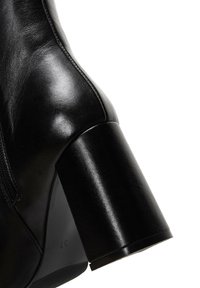Botte en cuir noir avec une texture lisse, bout arrondi et talon épais. La fermeture éclair latérale ajoute un détail fonctionnel. Taille 37 marquée sur la semelle.