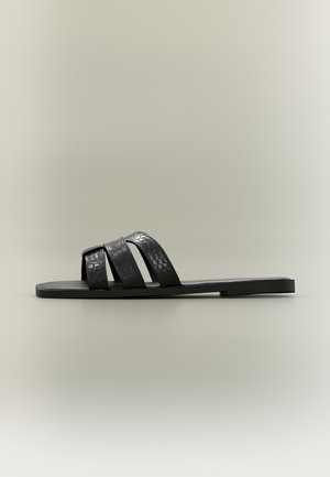 Sandale plate noire avec trois brides texturées au motif croco sur le dessus du pied et une semelle fine, vue de profil sur un fond neutre.