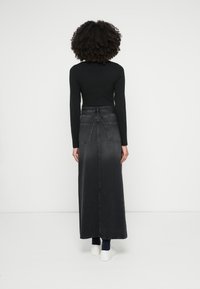 Maxi spijkerrok in donkergrijs met een aangesloten taille, zijzakken en een nette zoom. Gecombineerd met een zwart shirt met lange mouwen en witte sneakers.