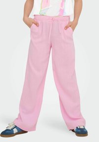 Pink wide-leg pants with a drawstring waistband, featuring side pockets and a lightweight texture, paired with blue sneakers.