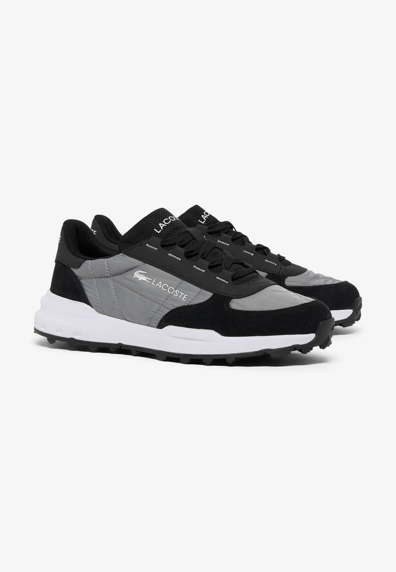 Paire de baskets Lacoste grises et noires avec semelles blanches et lacets noirs, présentées côte à côte sur un fond blanc.