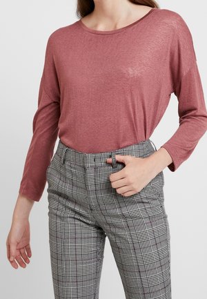 Camicia a maniche lunghe in rosa polveroso, realizzata in tessuto leggero, abbinata a pantaloni a quadri a vita alta in nero, bianco e grigio.