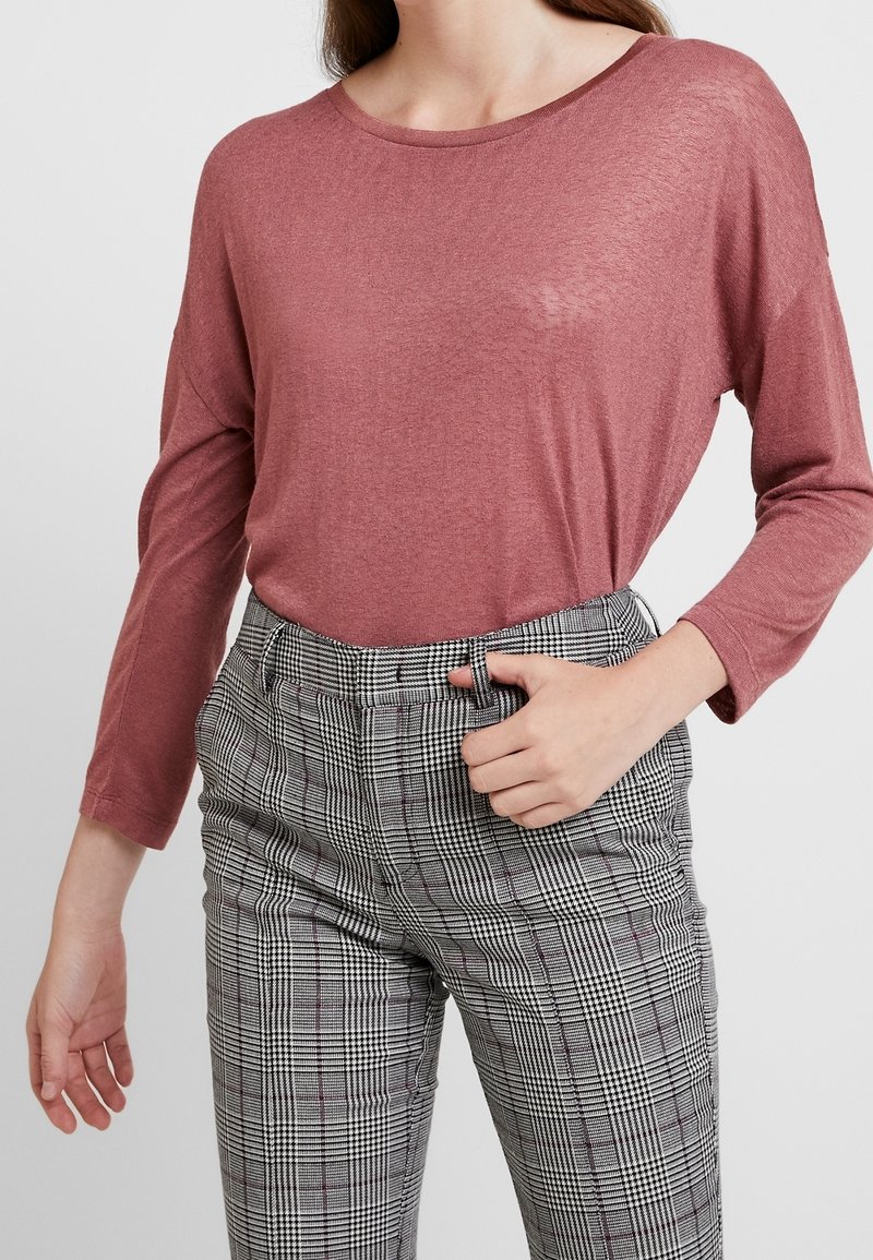 Camicia a maniche lunghe in rosa polveroso, realizzata in tessuto leggero, abbinata a pantaloni a quadri a vita alta in nero, bianco e grigio.