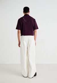 Kortermet, mørkerød rutete skjorte med krage og broderte detaljer, pairt med løstsittende, off-white bukser. Enkelt design.