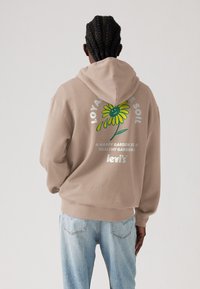 Beige hoodie met een groen en geel bloemenpatroon op de achterkant, voorzien van tekst en het Levi's-logo. van katoen, ontspannen pasvorm.