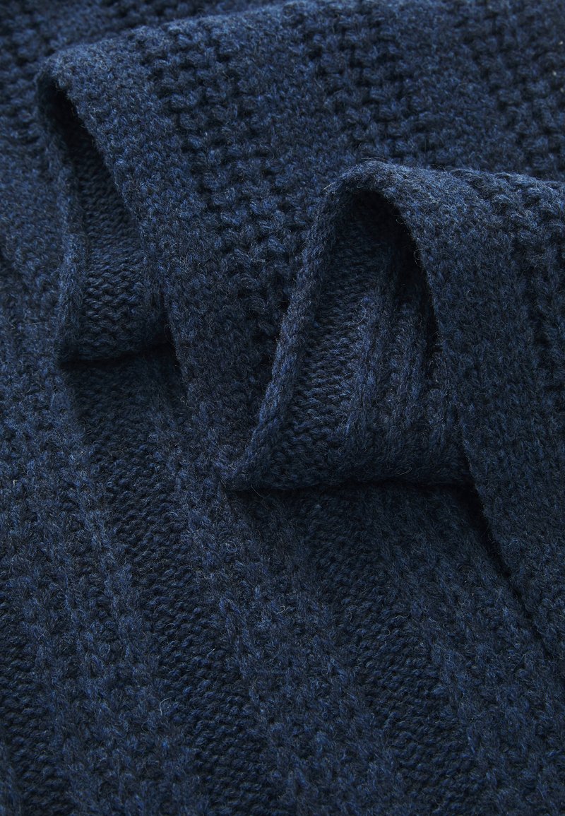 Diepblauwe gebreide stof met een getextureerd kabel- en wafelpatroon, gepresenteerd in een gevouwen staat met zichtbare zachte, wollen vezels.