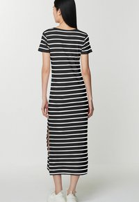 Robe maxi à rayures noires et blanches avec des manches courtes, des fentes latérales et un col rond. Fabriquée en tissu doux et avec une coupe décontractée.