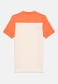 Kortermet idrettsskjorte med oransje øvre del og lys ferskenfarge nederst, med nettstruktur; inkluderer en subtil logodetalj.