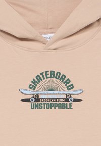 Μπεζ φούτερ με γραφικό σκιτσαρίσματος skateboard και κείμενο "SKATEBOARD UNSTOPPABLE New York City Brooklyn Team" στο στήθος.