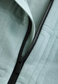 Lyseblåt stof med et tekstureret mønster, med en sort lynlås langs kanten og en mærkepræget lynlåstrækker.