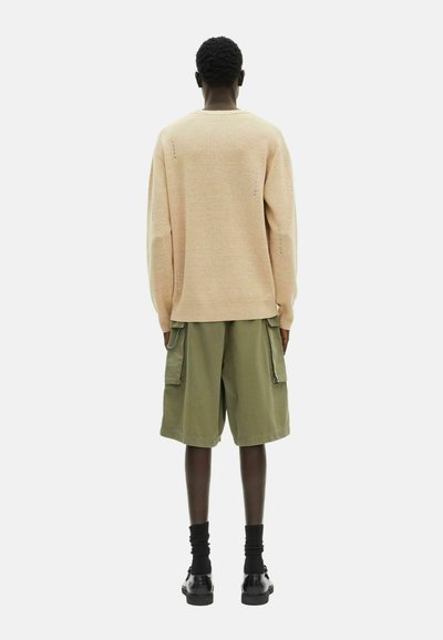 Beige gestrickter Pullover, olivgrüne Cargo-Shorts, schwarze Socken, glänzende schwarze Schuhe; sichtbare Nähedetails am Pullover; lässige Passform.