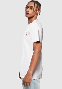 T-shirt en coton blanc avec un graphique rouge sur la partie gauche de la poitrine. Manches courtes et coupe régulière.