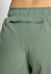 Grønne atletiske shorts med en teksturert overflate, med en liten glidelåslomme og en elastisk midje for en komfortabel passform.