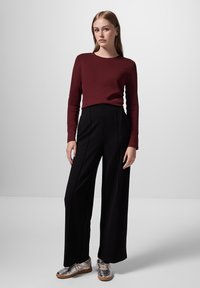 Vínová dlouhá halenka v kombinaci s černými širokými kalhotami; stříbrné tenisky s černými a bílými pruhy; hladké textury; přiléhavý design.