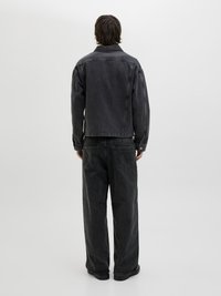 Giubbotto e pantaloni in denim nero, taglio rilassato. Il giubbotto ha un colletto ed è sbottonato, con cuciture visibili. Texture liscia, dettagli minimi.