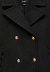 Abrigo negro de doble botonadura con botones dorados, solapas con muesca y tejido de lana texturizada. Cuenta con bolsillos laterales y costuras entalladas.