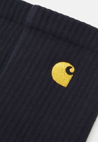 Marineblå ribbestrikkede sokker lavet af blødt stof, med et gult broderet logo, rundet design og subtil tekstur.
