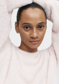 Jasnoróżowy, puszysty sweter o miękkiej strukturze. Ręce postaci są uniesione, a na jej twarzy widać neutralny wyraz oraz piegi.