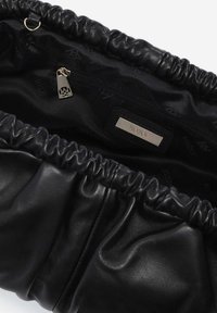 Czarna skórzana torebka o marszczonym wykończeniu i wewnętrznej kieszeni na zamek. Podszewka z czarnej tkaniny z delikatnym wzorem logo. Detale w kolorze srebrnym.