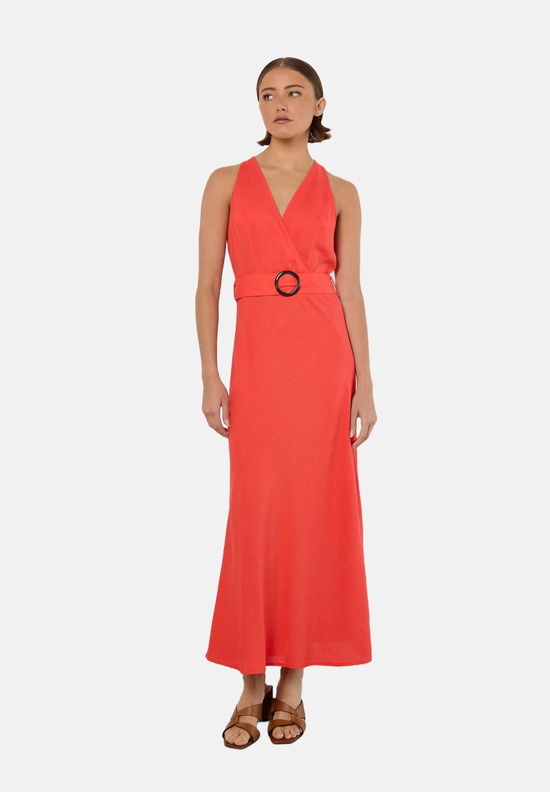 Robe maxi corail avec un décolleté en V et une ceinture à boucle circulaire. Texture lisse et design long jusqu'au sol, associée à des sandales marron.